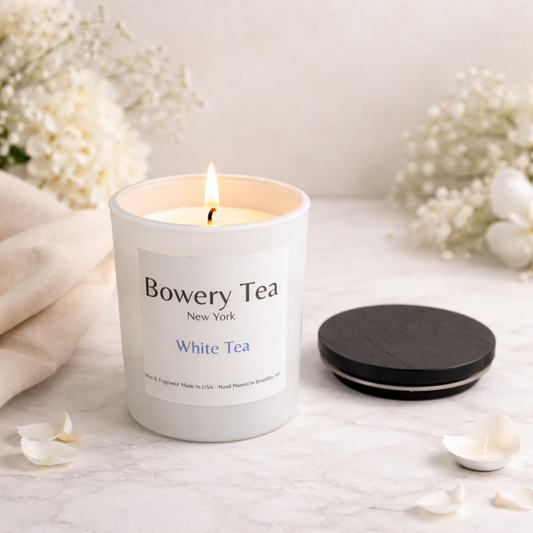 Bowery Tea candle on a white surface with flowers in the background