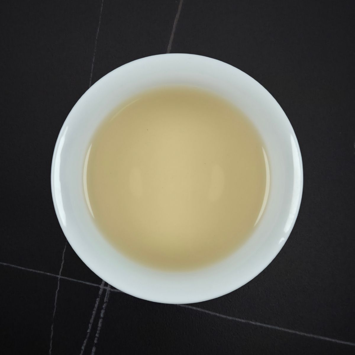White bowl with beige liquid on a black tiled floor