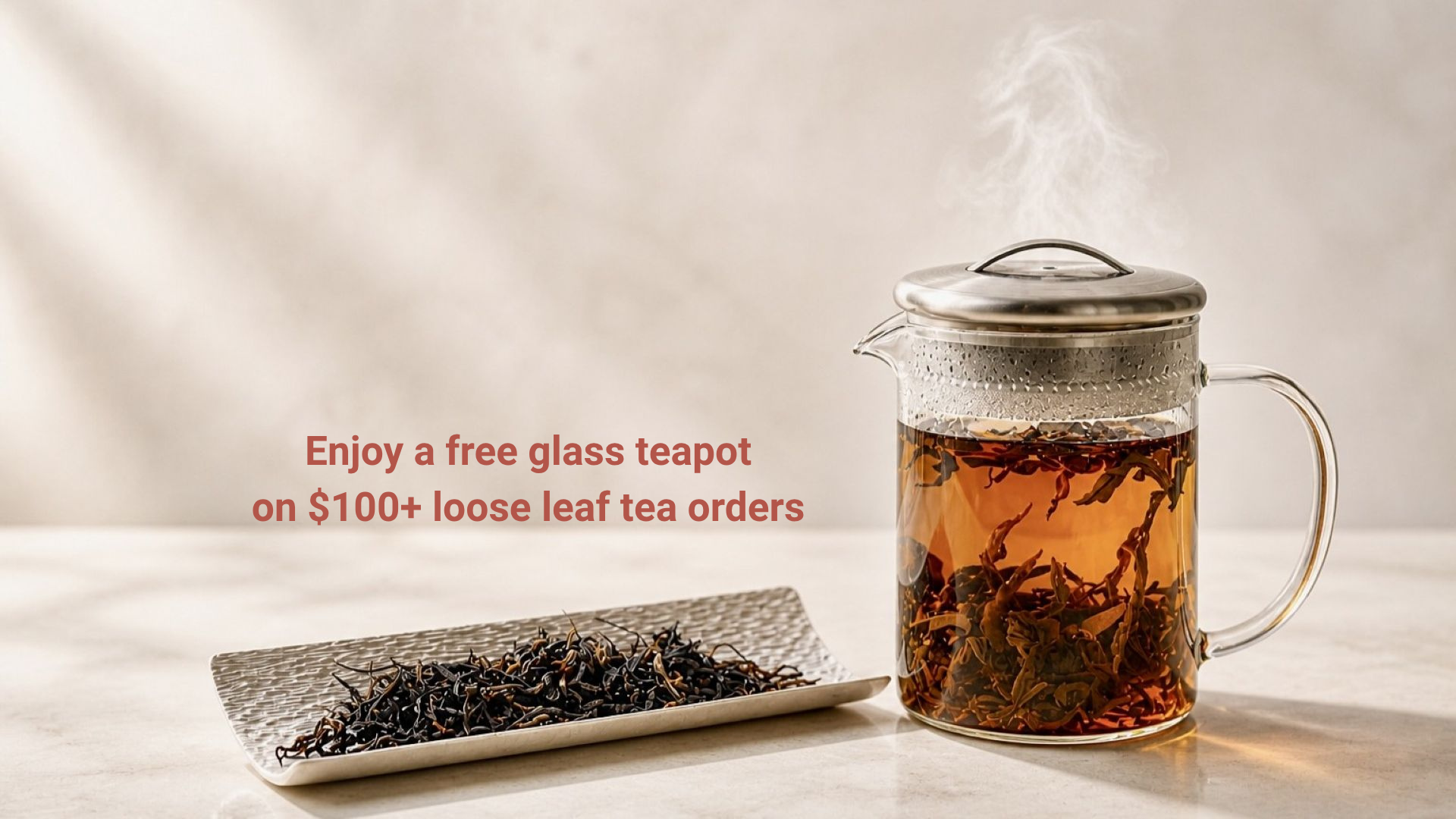 Glass teapot with steaming tea on a white surface, accompanied by loose leaf tea.