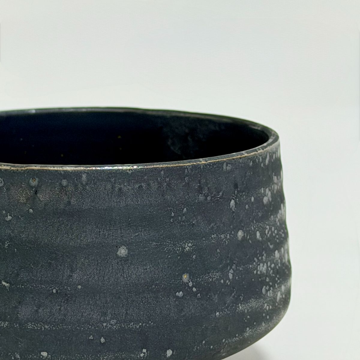 Close-up of a dark charcoal gray ceramic bowl with a textured, speckled glaze and a smooth rim, set against a plain light gray background.