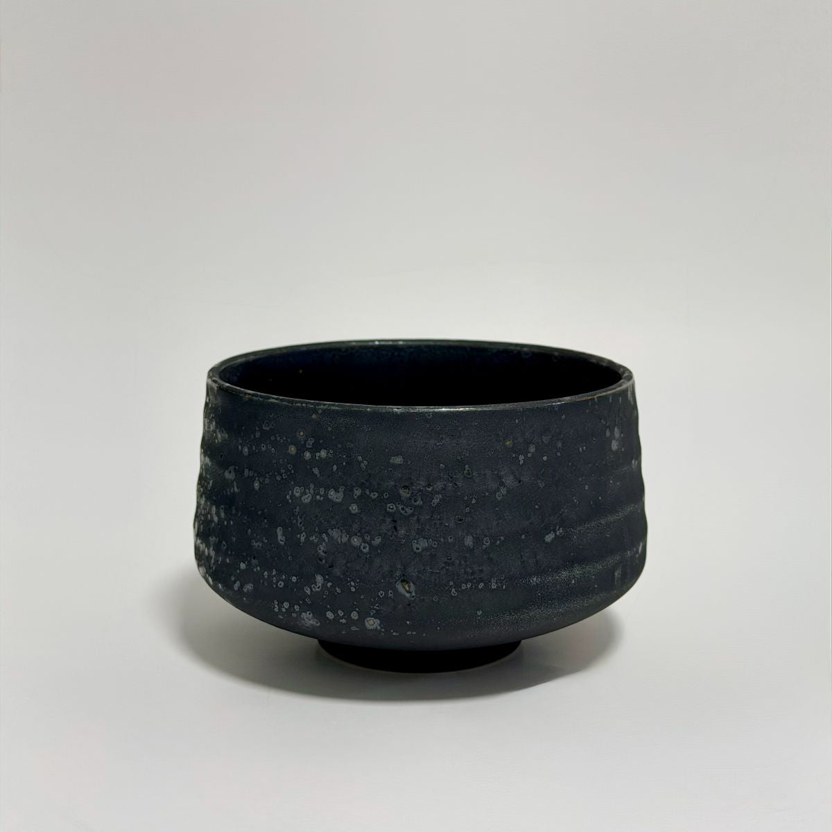 A dark charcoal gray ceramic bowl with a textured, speckled glaze, photographed against a neutral light gray background.