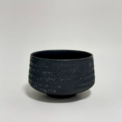 A dark charcoal gray ceramic bowl with a textured, speckled glaze, photographed against a neutral light gray background.