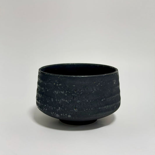 A dark charcoal gray ceramic bowl with a textured, speckled glaze, photographed against a neutral light gray background.