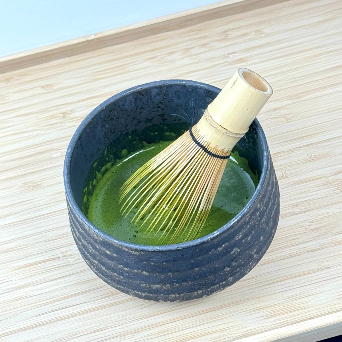 Matcha green tea in a bowl with a whisk on a light wooden surface