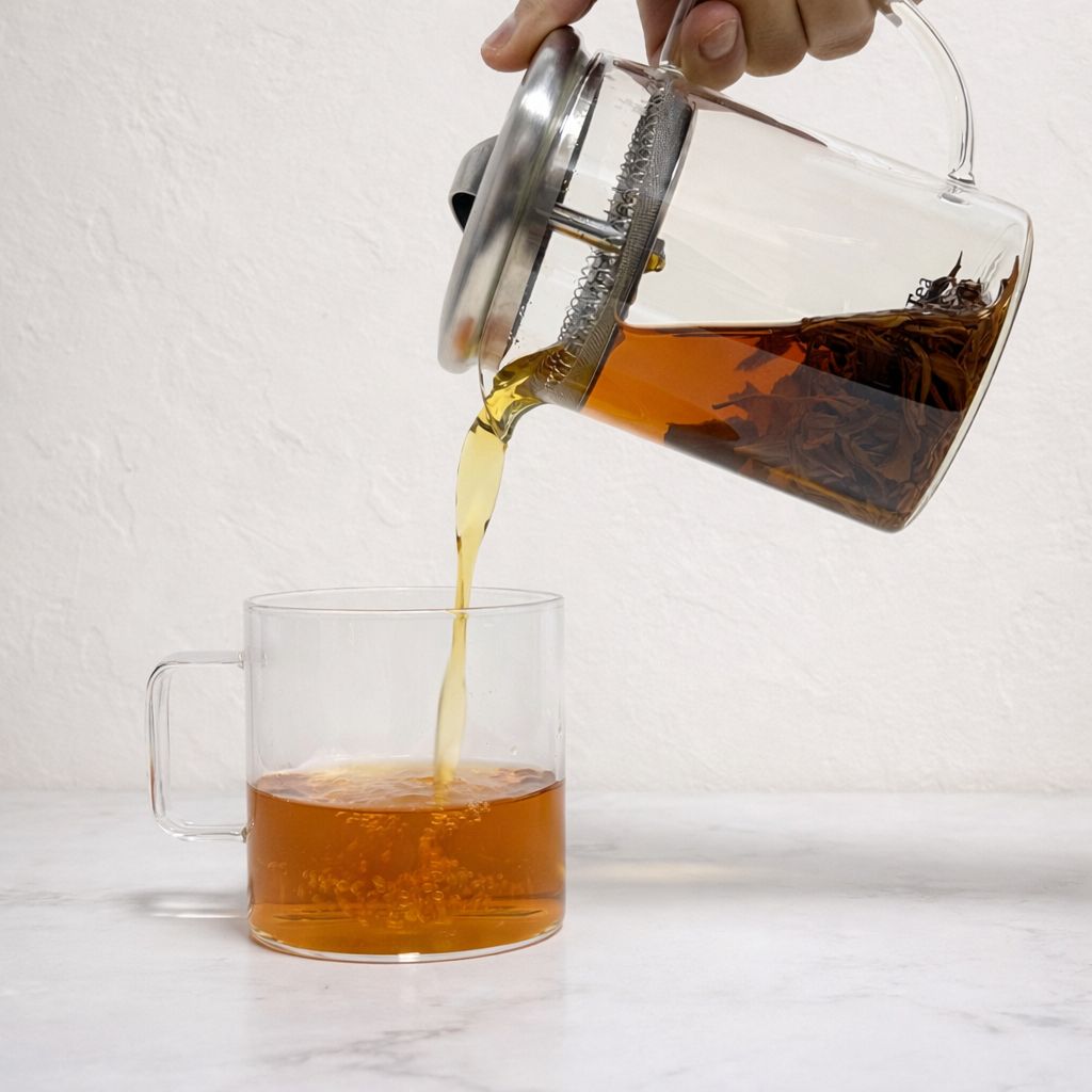 Tea being poured from a glass teapot into a cup, demonstrating western-style brewing