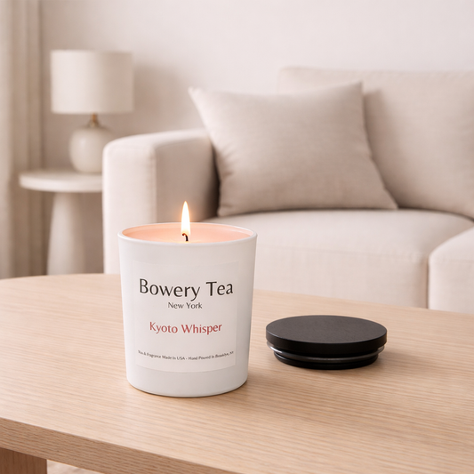 Bowery Tea Kyoto Whisper scented candle lit in white glass jar with wooden lid beside it