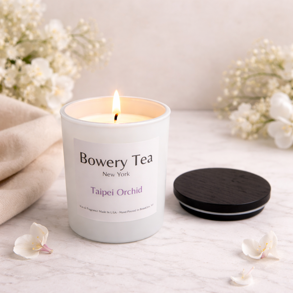 Bowery Tea Taipei Orchid scented candle lit in white glass jar with wooden lid beside it