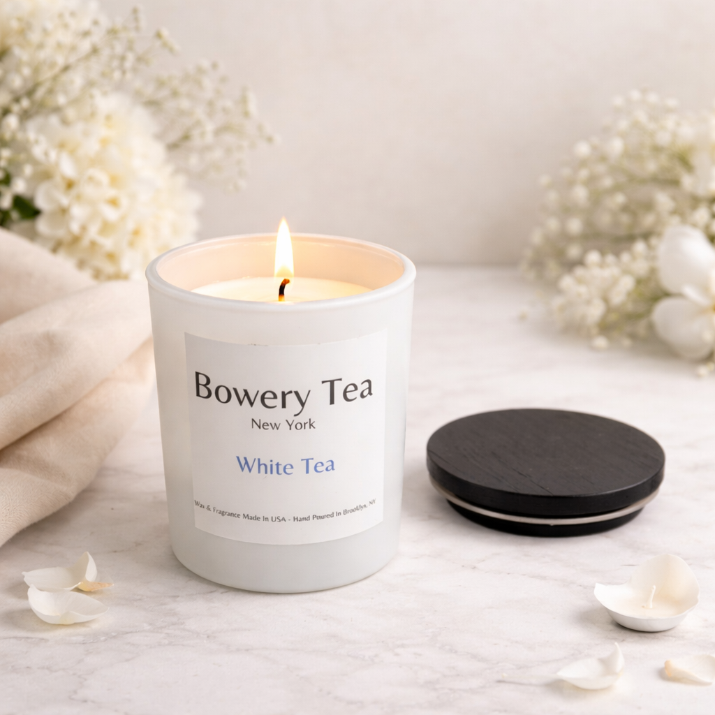 Bowery Tea candle on a white surface with flowers in the background