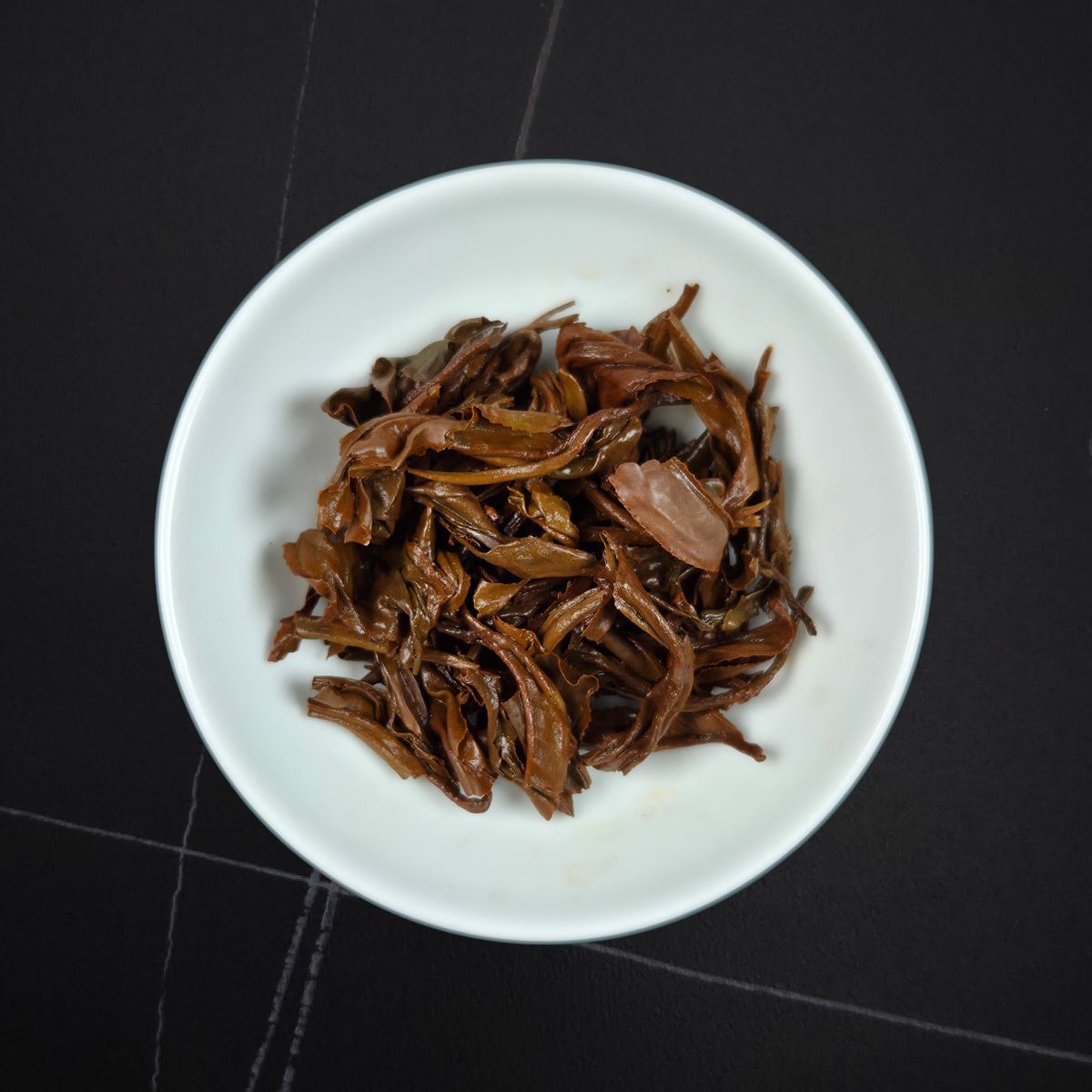 Golden Honey black tea wet spent leaves — unfurled reddish-brown leaves in a white dish