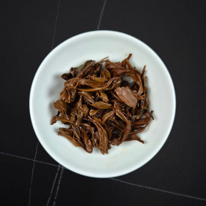 Golden Honey black tea wet spent leaves — unfurled reddish-brown leaves in a white dish