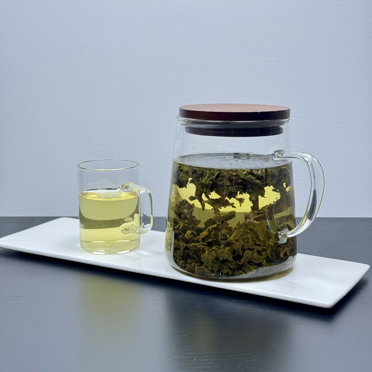 Glass pitcher of tea leaves steeping in cold water with a cup beside it