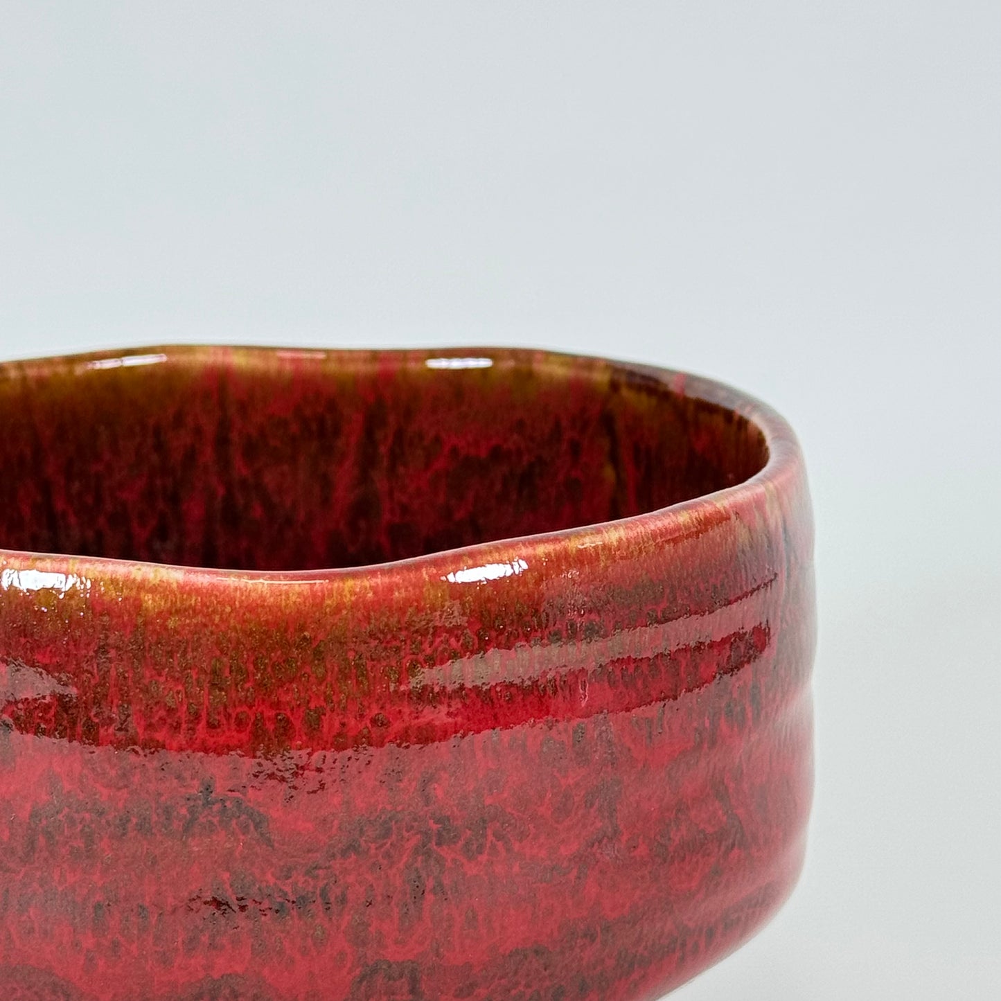 Close-up of crimson glazed Japanese chawan with textured surface and layered red tones