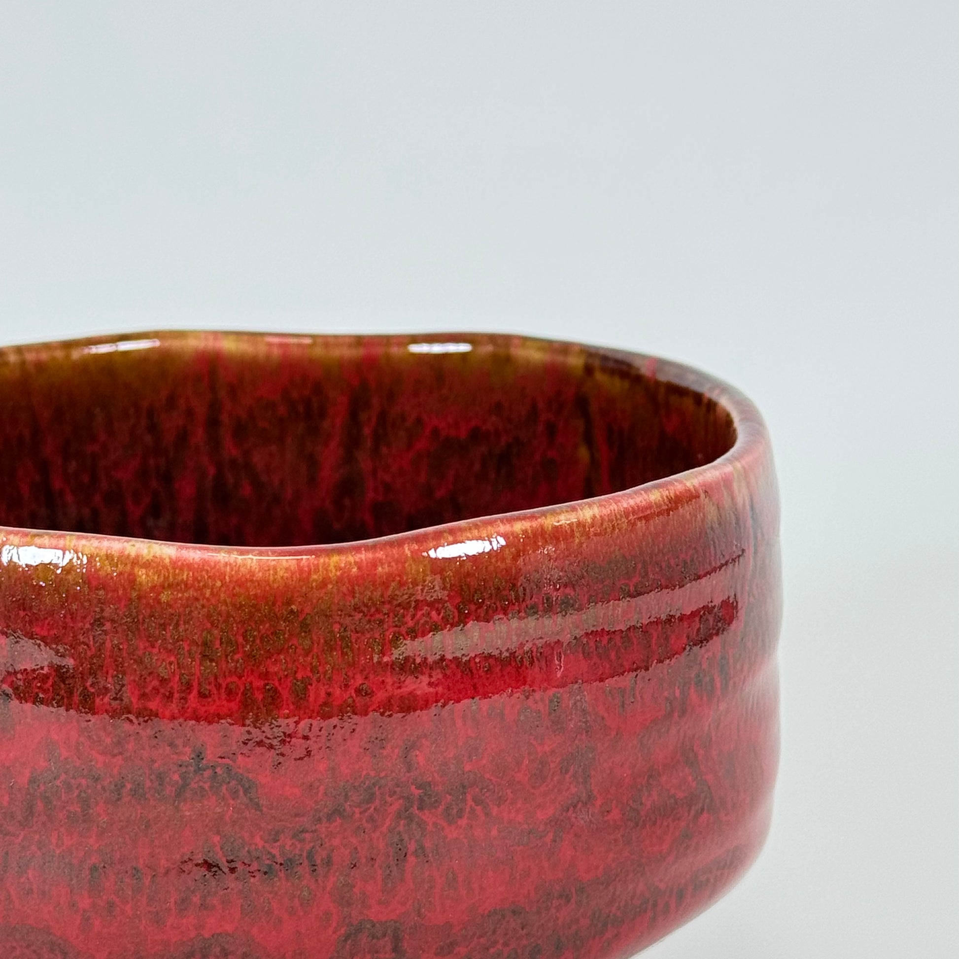 Close-up of crimson glazed Japanese chawan with textured surface and layered red tones