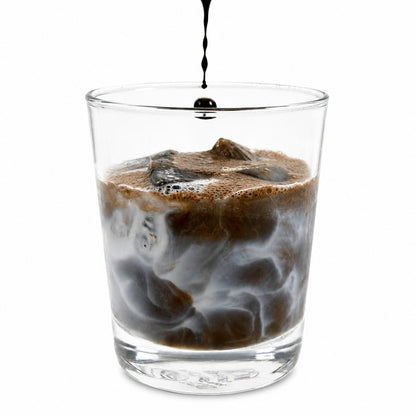Glass of iced coffee with a stream of liquid being poured on a white background