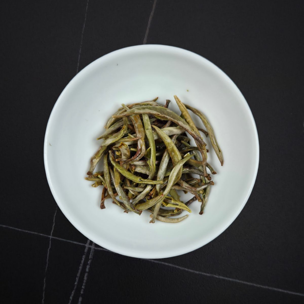 Wet Imperial Silver Needle white tea leaves after brewing in a white tasting cup