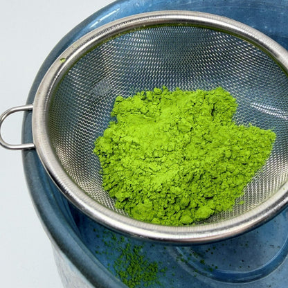 Green powder in a metal sieve on a blue container