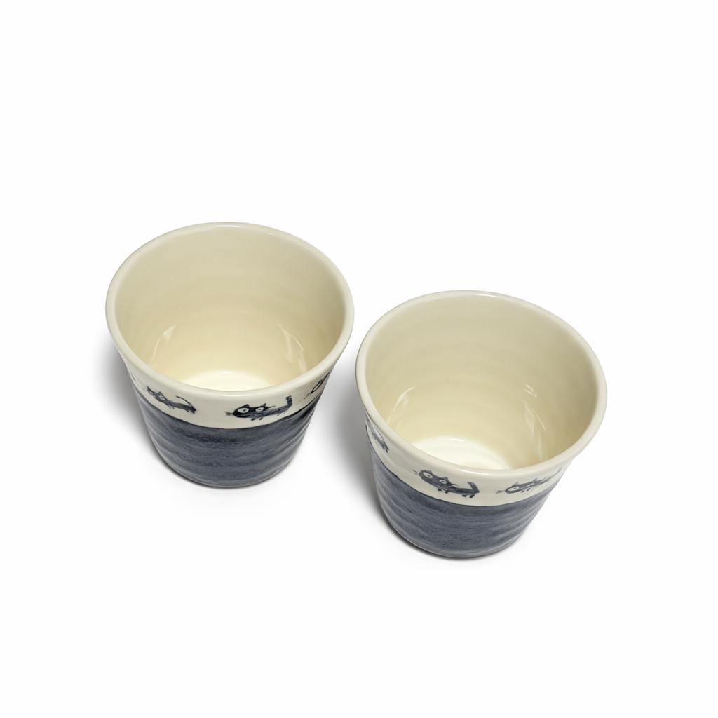 Set of two porcelain teacups with black cat illustrations ivory interior and charcoal glaze top view