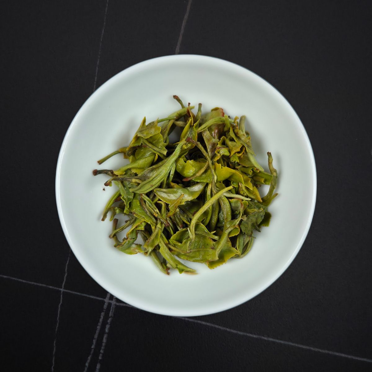 Wet Mao Feng green tea leaves after brewing in a white tasting cup