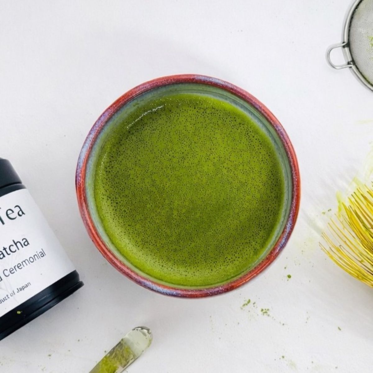 Bowl of whisked matcha with bamboo whisk and tools arranged on a surface
