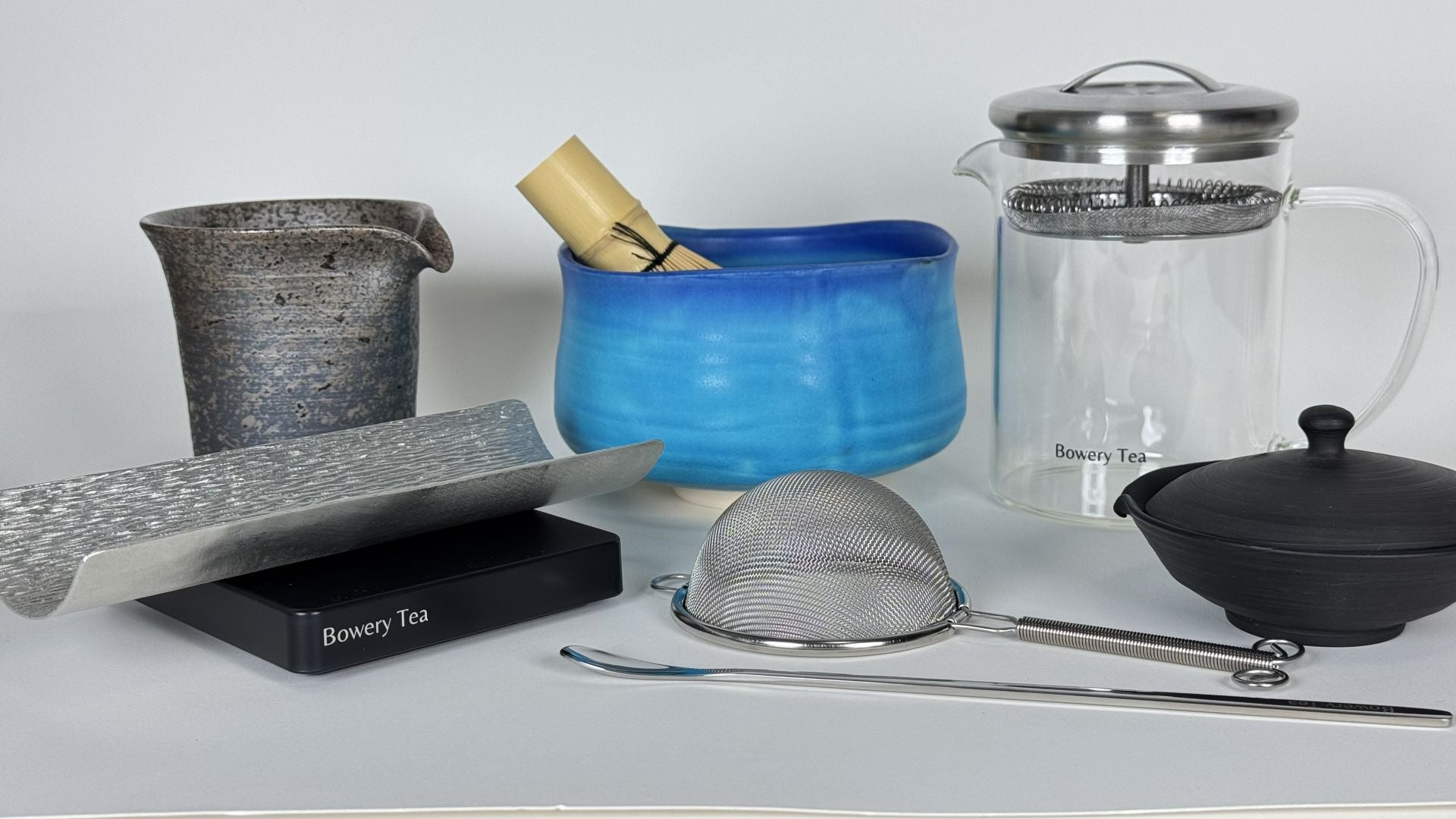 Collection of teaware including teapot, strainer, whisk, and cups used for preparing and serving tea